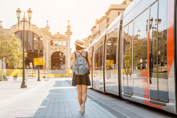 Junge Frau mit Rucksack neben einer Straßenbahn
